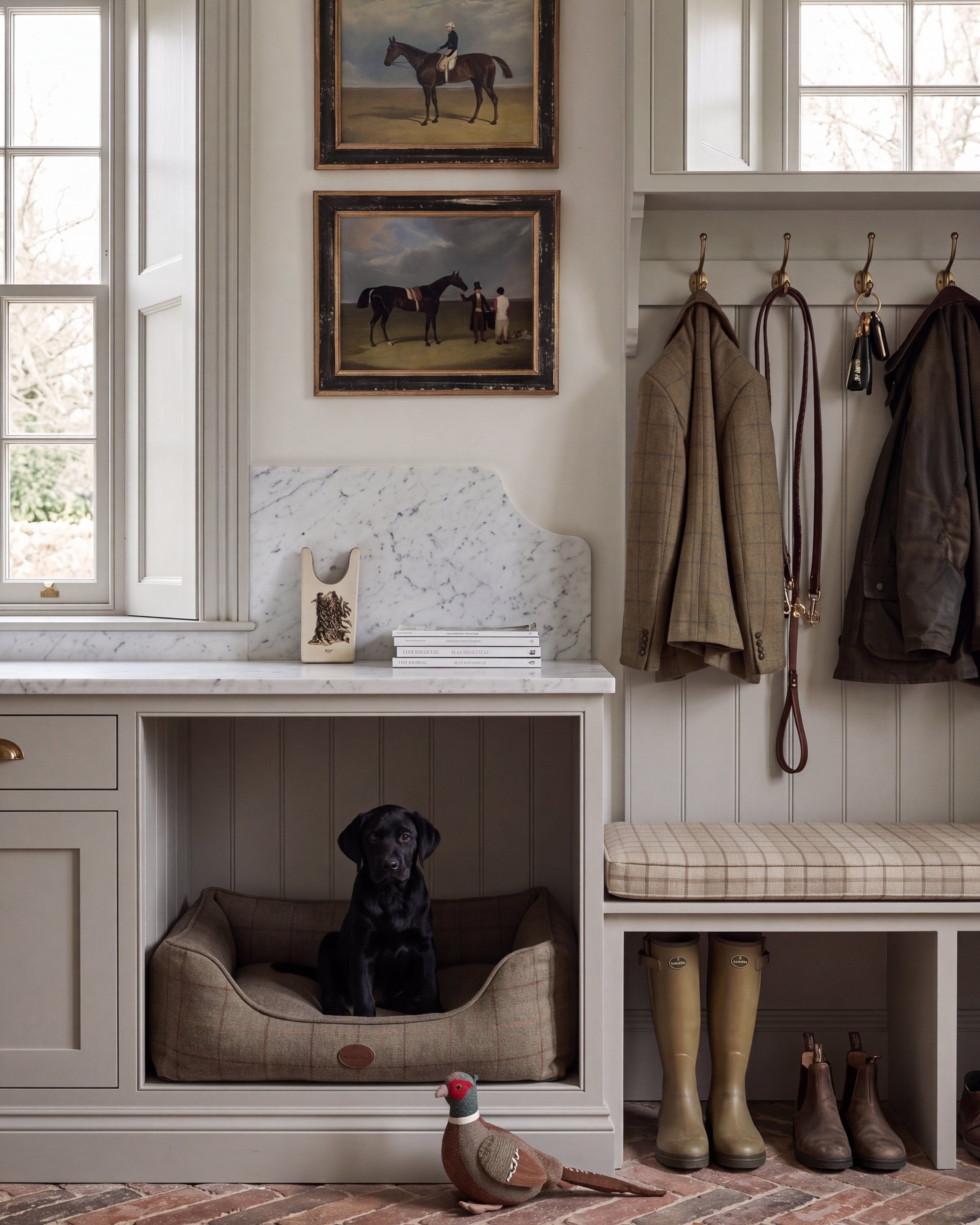 Cosy English country boot room with a black Labrador puppy, tweed furnishings and wellington boots, the antique-style interior behind Pretty in Print Art's vintage framed art collection