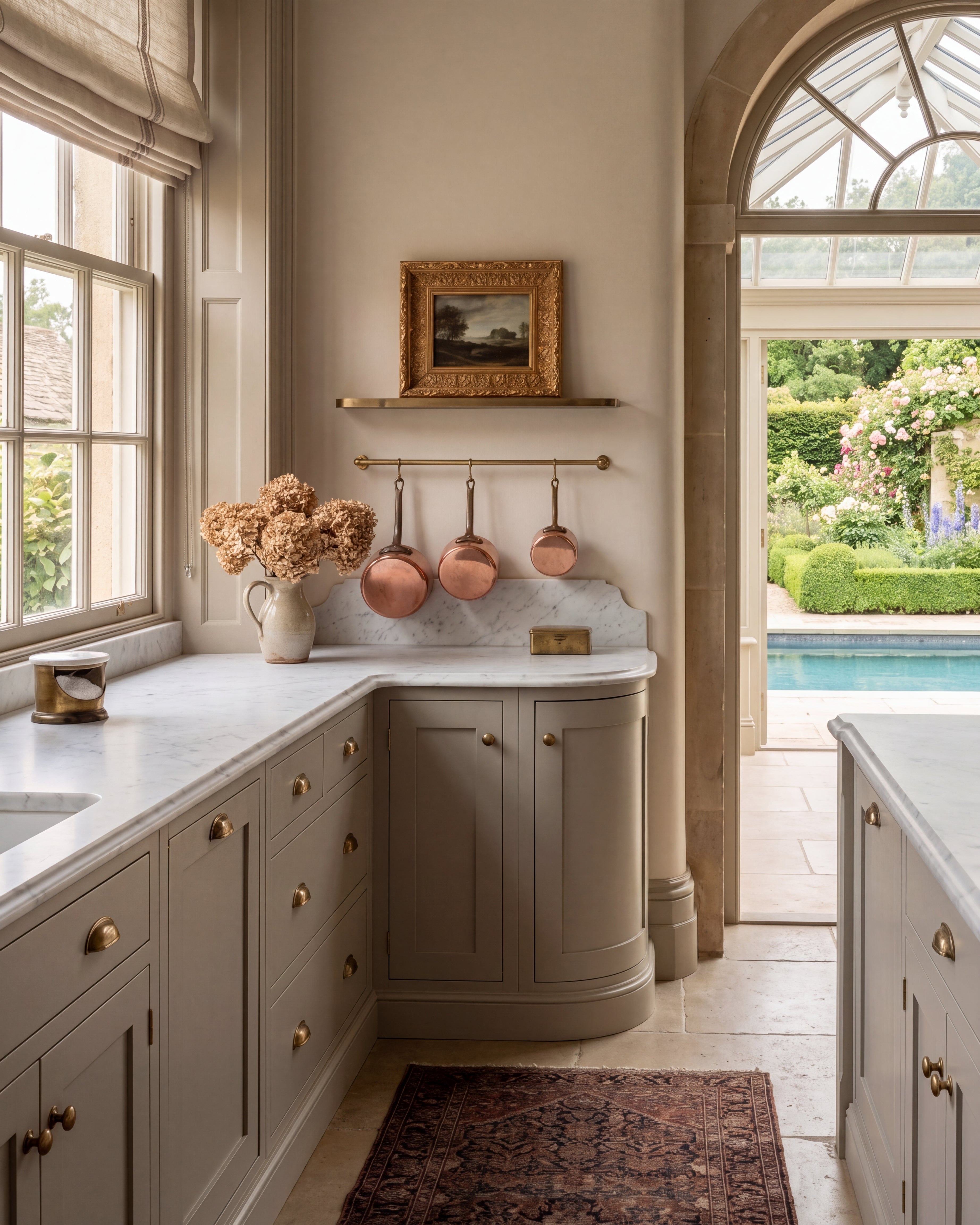 A framed antique oil painting print in an ornate gold frame displayed on a kitchen shelf above hanging copper pans and marble countertops