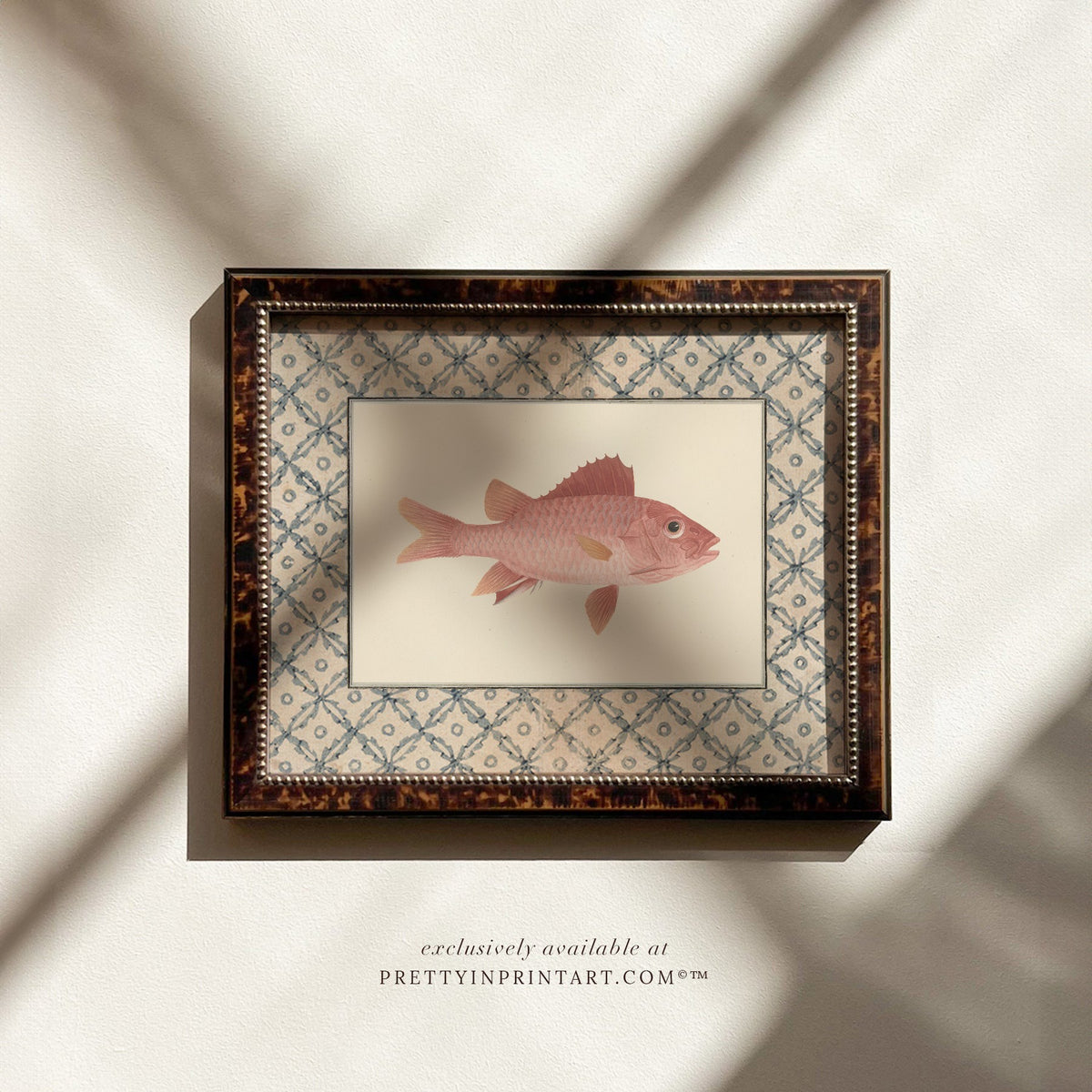Vintage coral-pink fish art print with a blue lattice border in a tortoiseshell-style wooden frame, ideal for a coastal bathroom or cottage kitchen