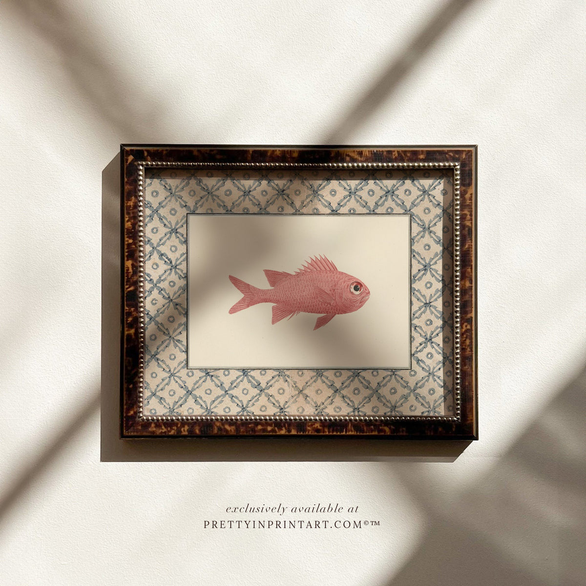 Vintage rosy pink fish art print with a blue lattice border in a tortoiseshell-style wooden frame, ideal for a coastal bathroom or cottage kitchen
