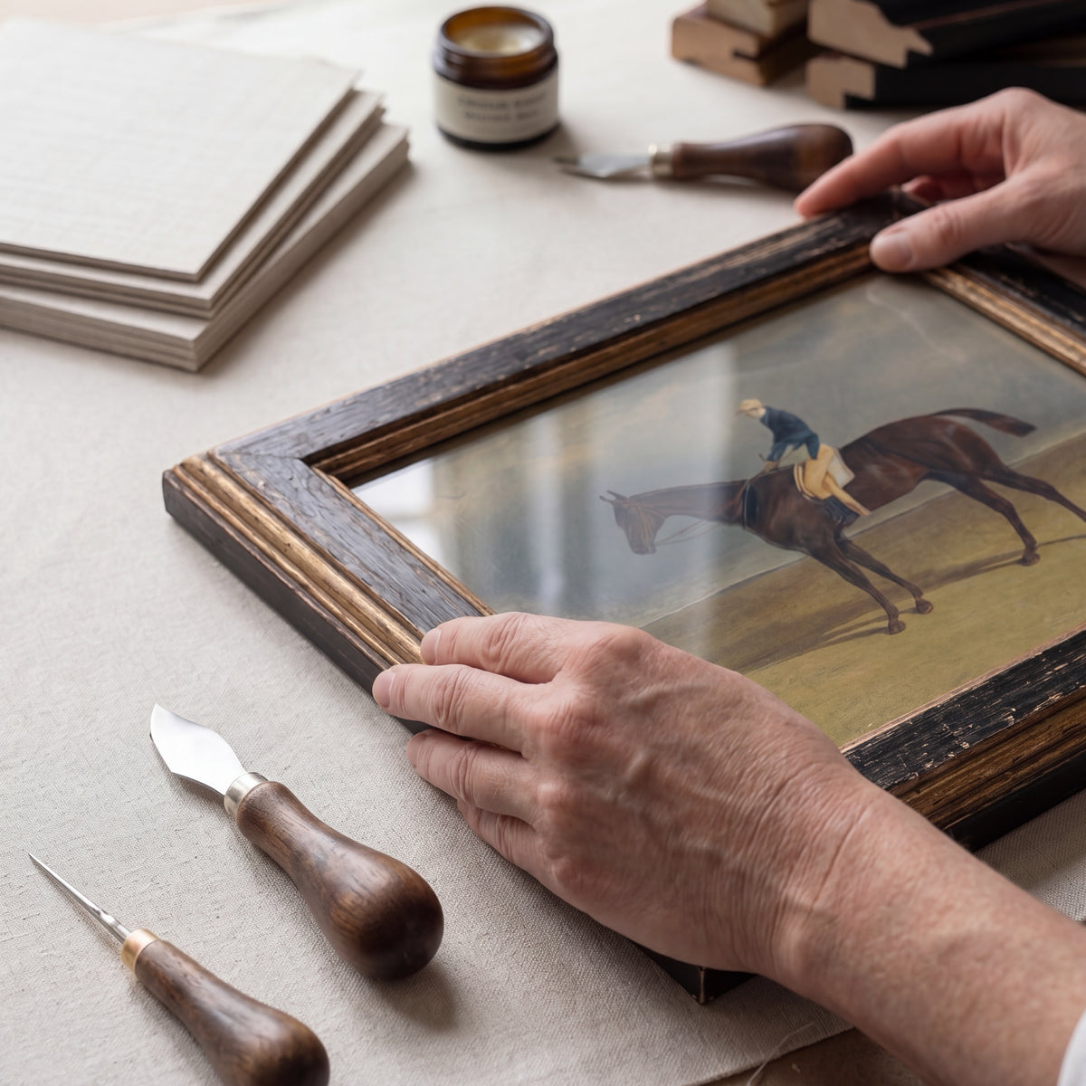Craftsperson hand-restoring a vintage horse and jockey painting in a British framing workshop
